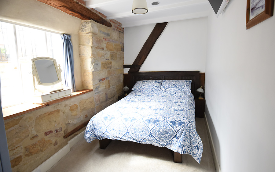 comfortable double bed, one stone wall with window facing Cliff Street, one wall with timber beams of a former roof structure